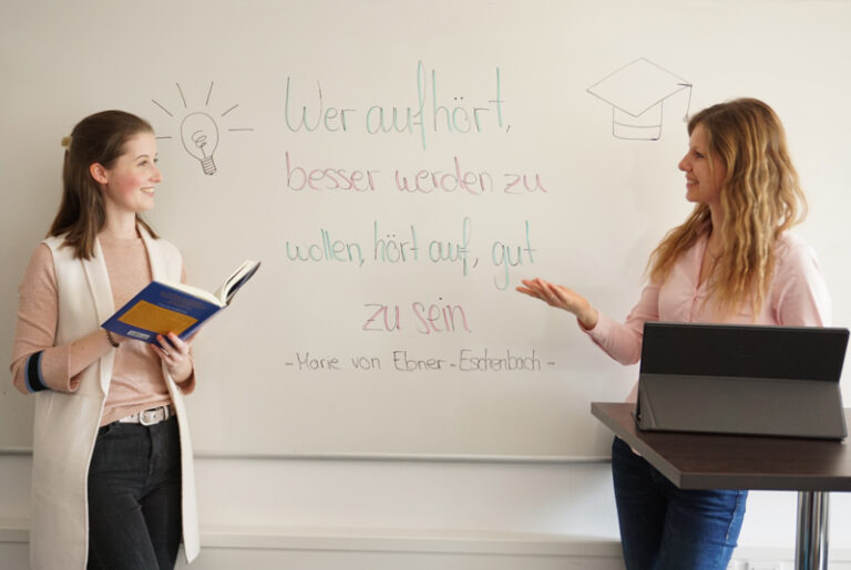 Zwei Kolleginnen am Whiteboard mit einem Zitat zur Weiterbildung