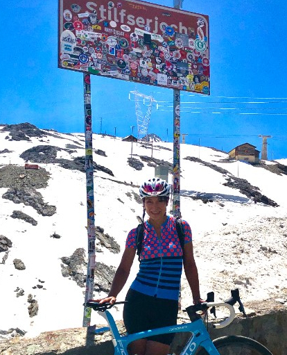 Mitarbeiterin mit Rennrad an einem Passschild im Schnee