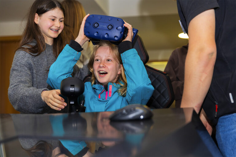 Mädchen setzt beim Girls'Day eine VR-Brille auf, begleitet von einer Mitarbeiterin