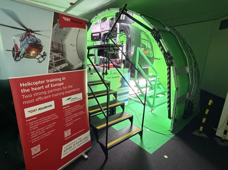 Grün ausgeleuchtetes Hubschrauber-Kabinen-Mock-up mit Infoplakat der DRF Akademie
