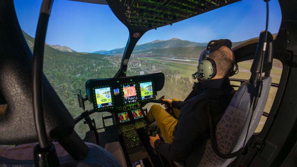 Pilot in the H145 cockpit of the Flight Training Device with an outside view of the terrain