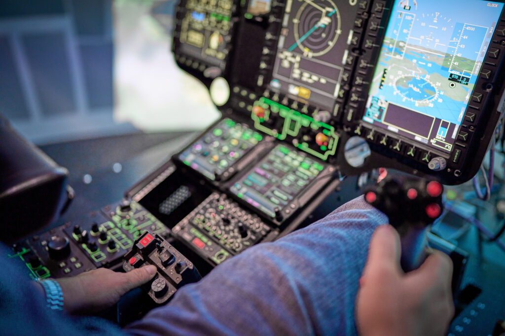 Pilot steuert im Cockpit eines Helikopter-Flugsimulators, Hand am Stick, aktive Displays