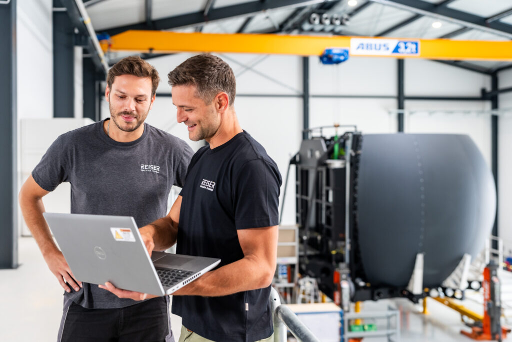 Zwei Kollegen prüfen mit dem Laptop einen Simulator in der Montagehalle